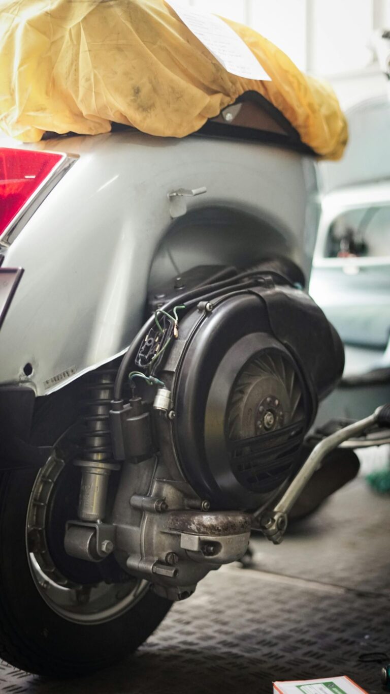 A detailed look at the rear wheel and engine of a scooter in a garage setting.